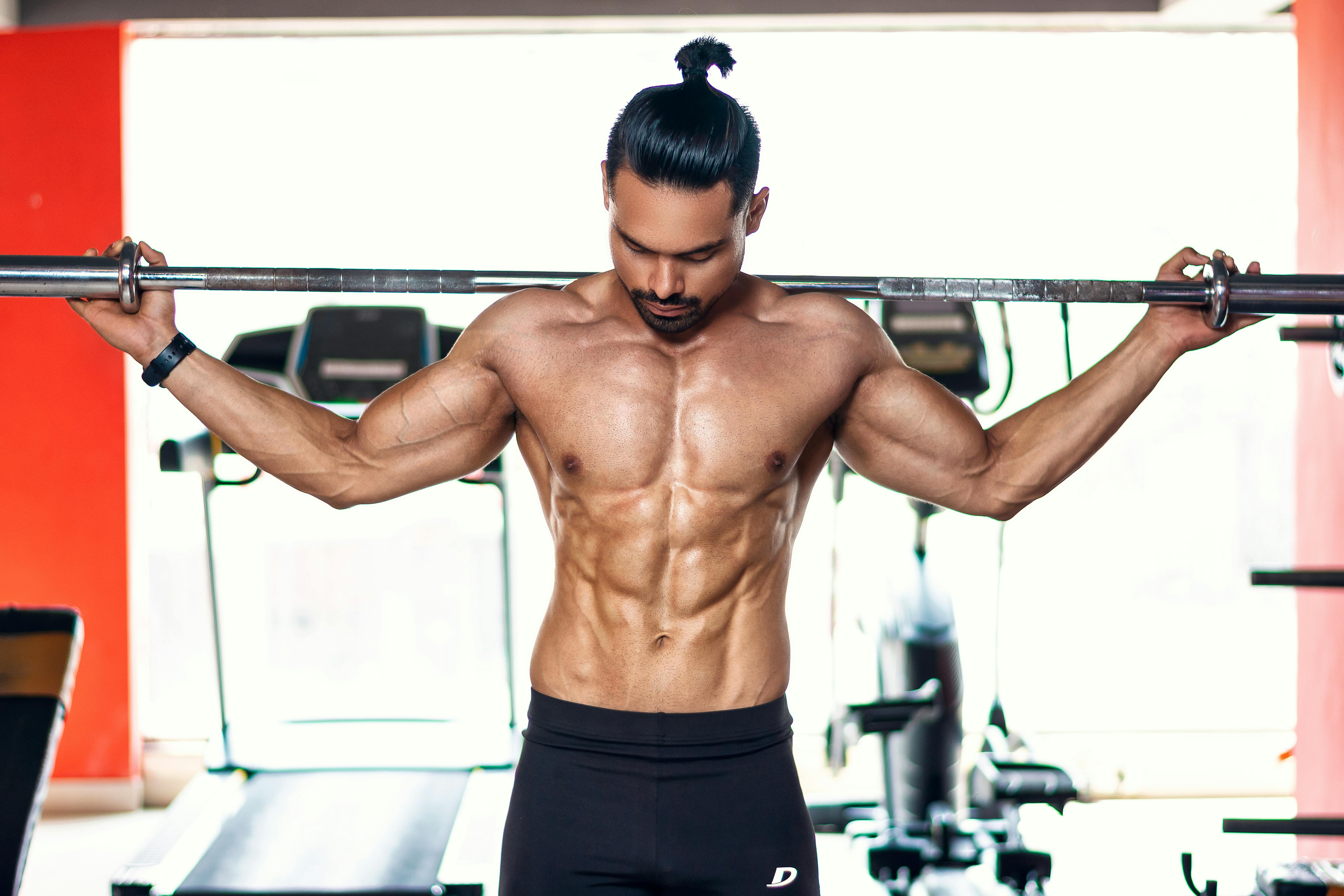 Strong and shirtless man lifting weights indoors in Pune gym.