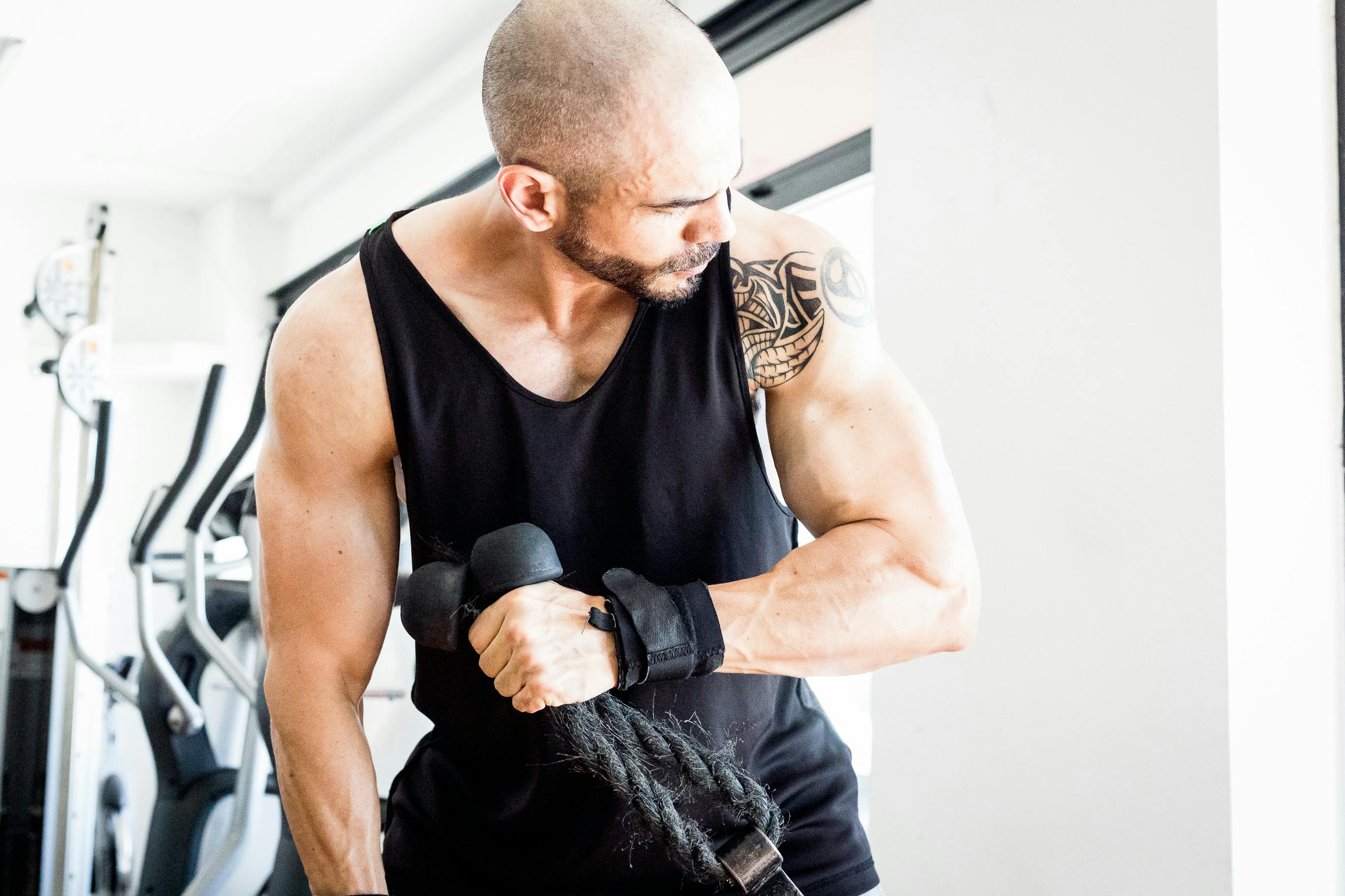 Bald man lifting rope weights, showcasing strength and tattoos in gym setting.